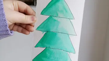 Hand holding watercolor tree drawing, indoors.