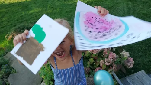 Child excitedly showing two colorful art pieces.
