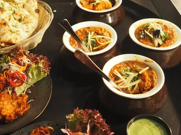Schalen mit indischem Essen, umgeben von Beilagen und Brot.