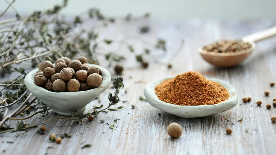 Bowls with whole and ground allspice on wooden table.