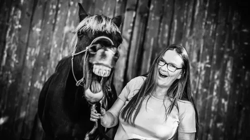 Woman with laughing horse in barn setting.