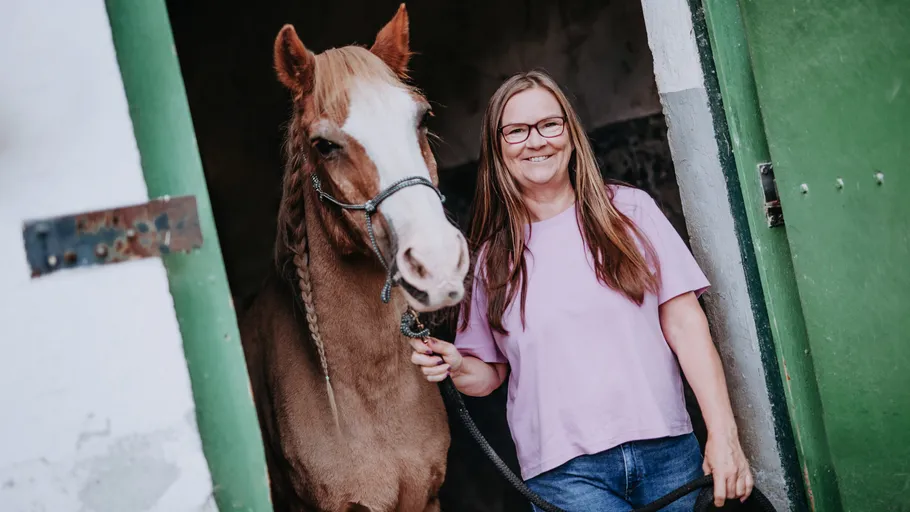 Woman smiling with horse in stable doorway.