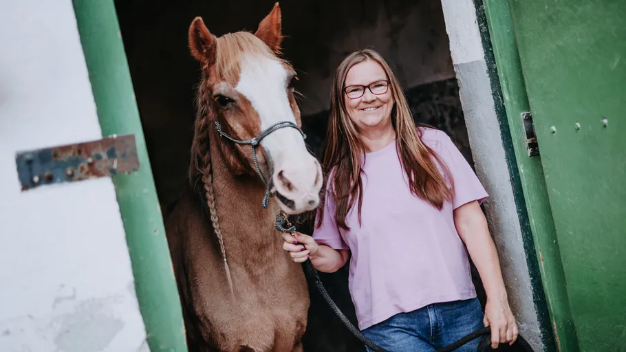 Woman smiling with horse in stable doorway.