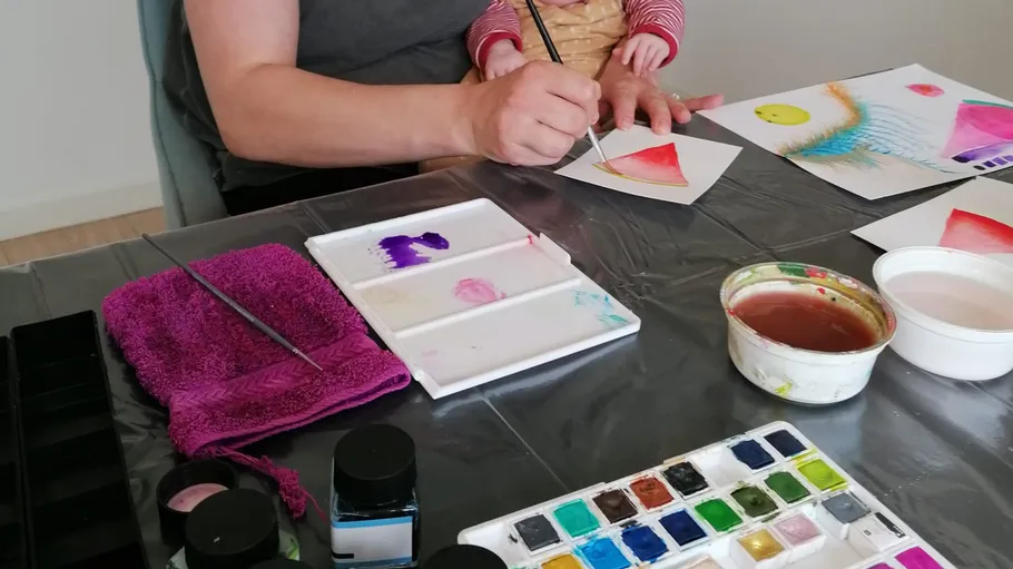 Person malt mit Kind an einem Tisch.