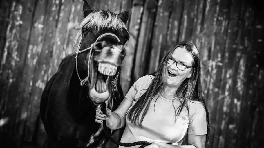 Frau mit Pferd lächelt neben Holzzaun.