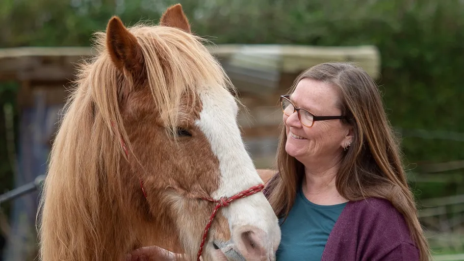 Woman smiling at horse in outdoor setting.
