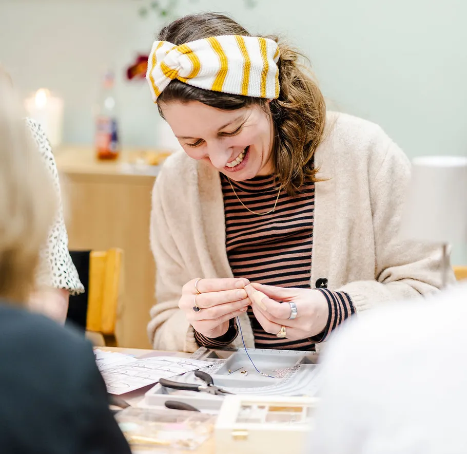 Woman smiling while crafting jewelry at table.