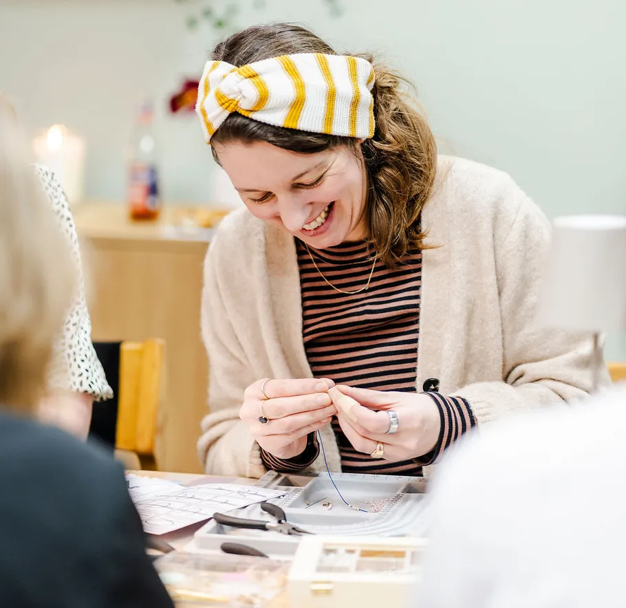 Woman crafting jewelry, smiling, indoor setting.