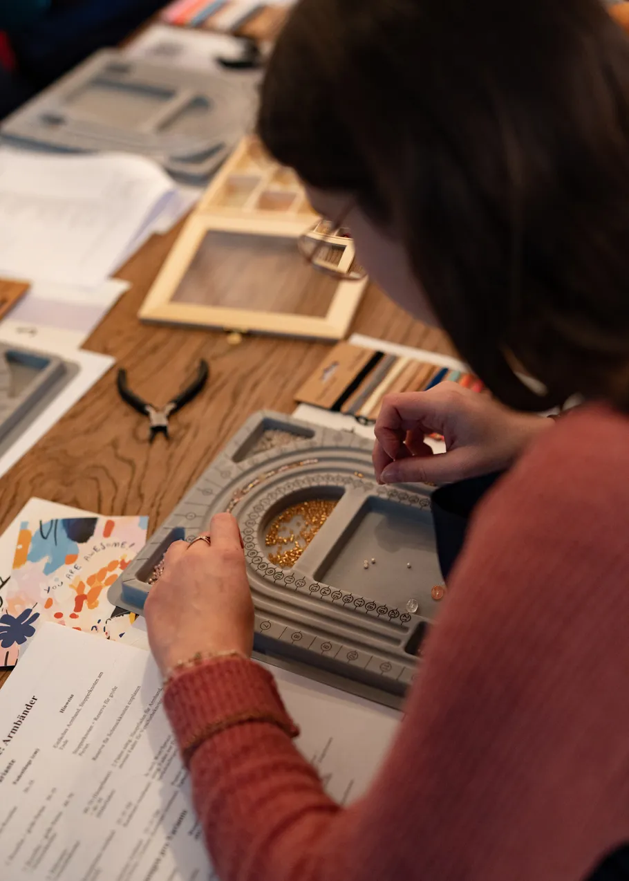 Person crafting jewelry at wooden table.