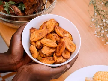 Eine Hand hält eine Schüssel mit gebratenen Bananenstücken.