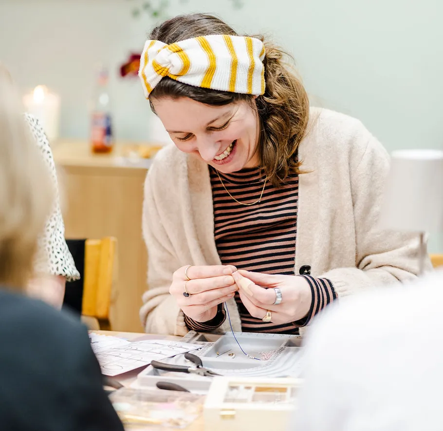 Woman crafting jewelry at a table, smiling.