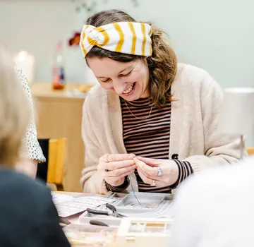 Woman crafting jewelry at workshop table.