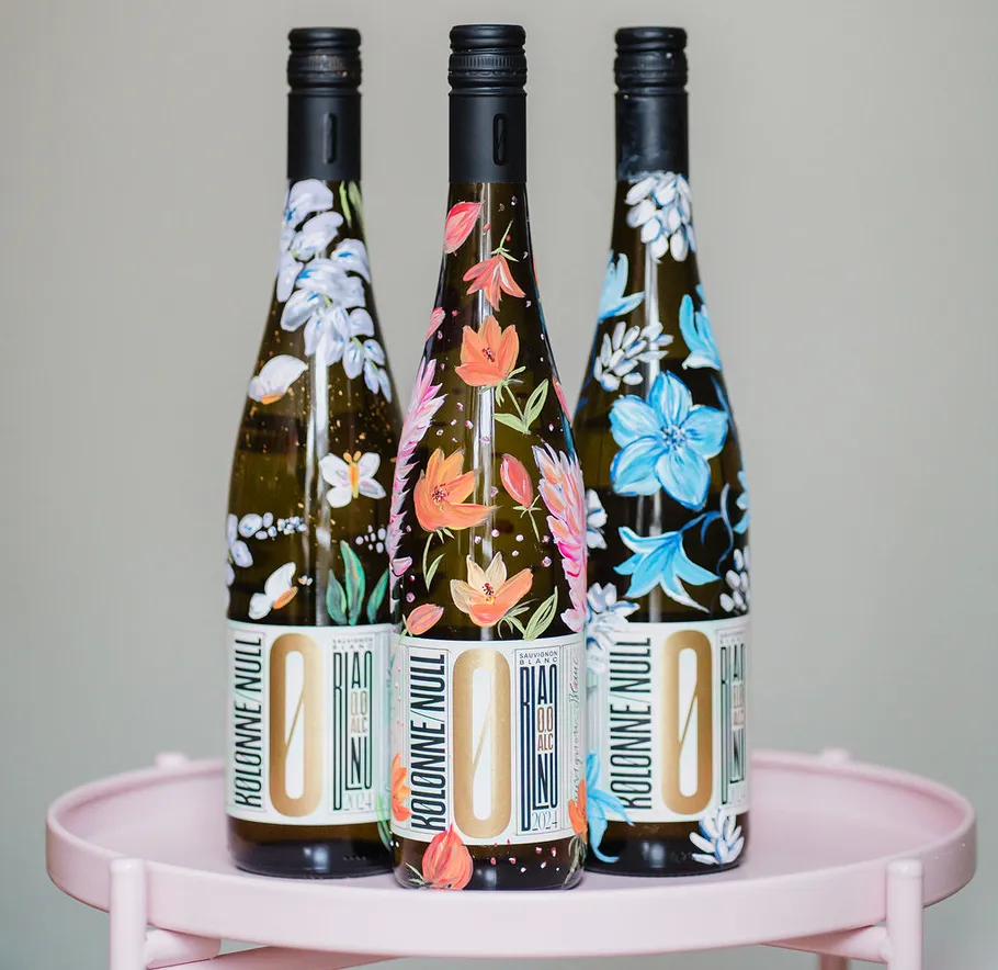 Three floral wine bottles on pink table.