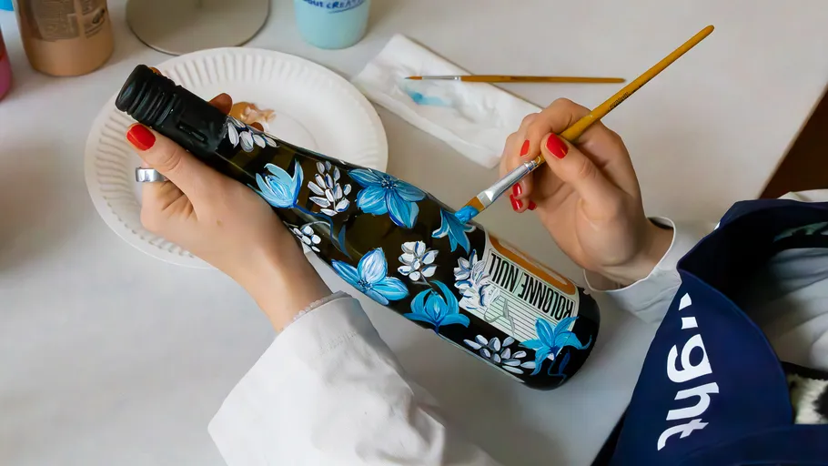 Person painting floral design on wine bottle.