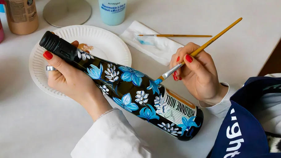 Person painting bottle with floral design.