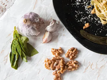 Knoblauch, Basilikum, Walnüsse und Pasta auf weißem Tisch.