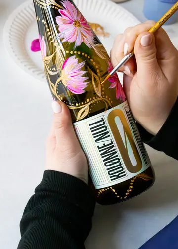 Person malt florales Design auf Flasche.