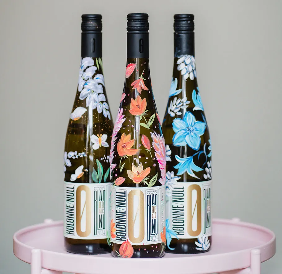 Three bottles with floral design on pink table.