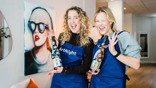 Two women smiling with decorated bottles indoors.