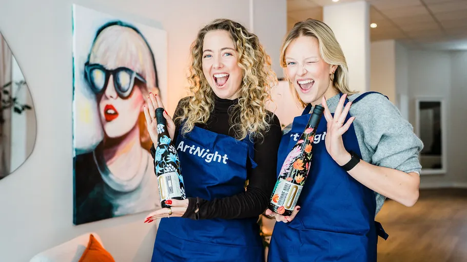 Two women smiling with decorated bottles indoors.