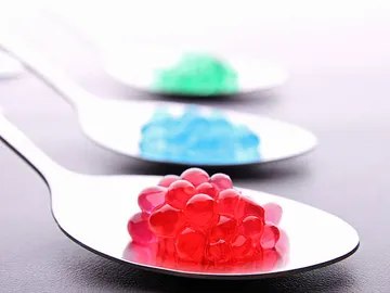 Löffel mit bunten, gelartigen Kügelchen auf einem Tisch.