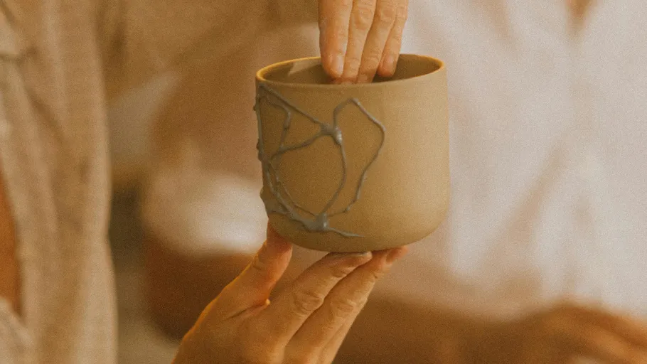 Hands holding a pottery cup indoors.