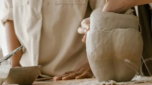 Hands molding clay vase on table.