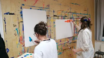 Two women painting abstract art on canvas.