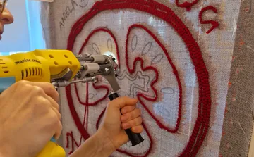 Person using tufting gun on fabric frame.