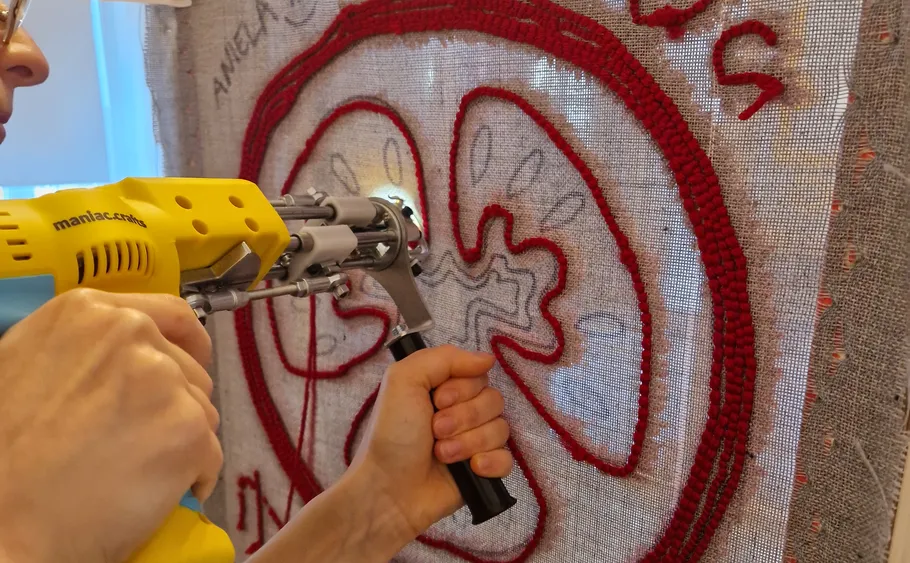 Person benutzt Tufting-Pistole auf Stoffrahmen.