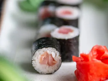 Sushirollen liegen auf weißem Teller neben eingelegtem Ingwer.