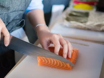 Koch schneidet Lachsfilet auf einem Schneidebrett.