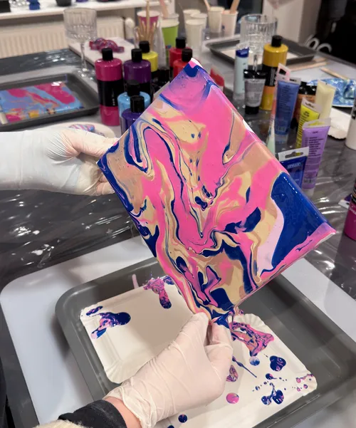 Hands tilt canvas with colorful paint swirls.