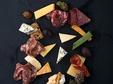 Käse und Wurst liegen auf einem schwarzen Brett angeordnet.