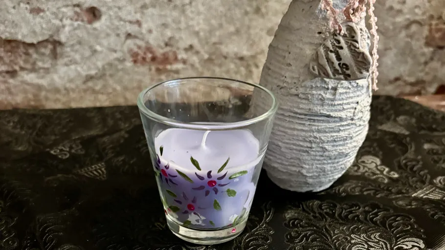 Purple candle in decorated glass beside ceramic vase.