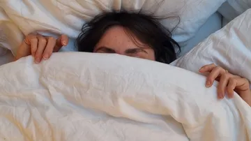 Person teilweise von weißer Bettwäsche bedeckt.