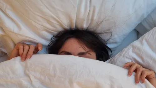 Person versteckt sich unter weißer Decke im Bett.