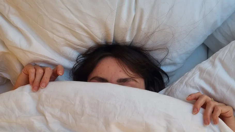 Person versteckt sich unter weißer Decke im Bett.