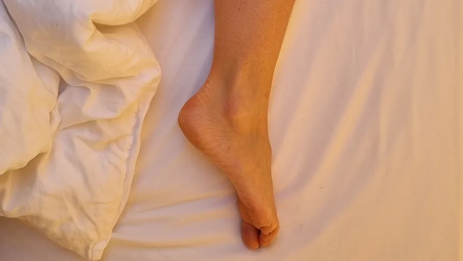 Foot resting on white bed sheets.
