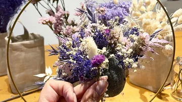 Hand arranging dried flowers in a frame.