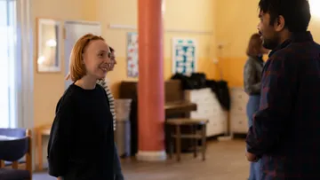 Two people smiling and talking indoors, cozy setting.