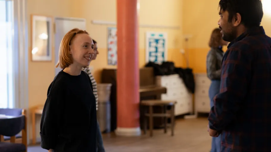 Two people smiling and talking indoors, cozy setting.
