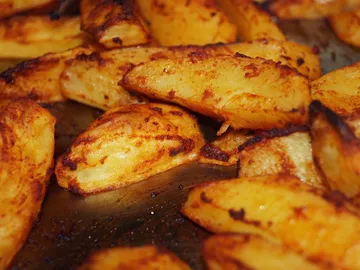 Fried pieces of potatoes are laid out on a baking sheet.