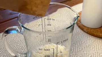 Pouring grains into measuring cup on table.