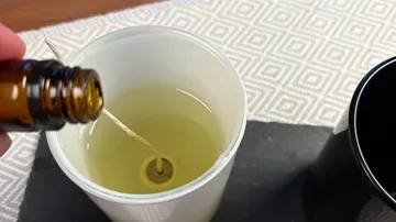 Pouring oil into candle holder with wick.