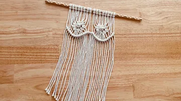 Macrame wall hanging on a wooden stick over a wooden background.