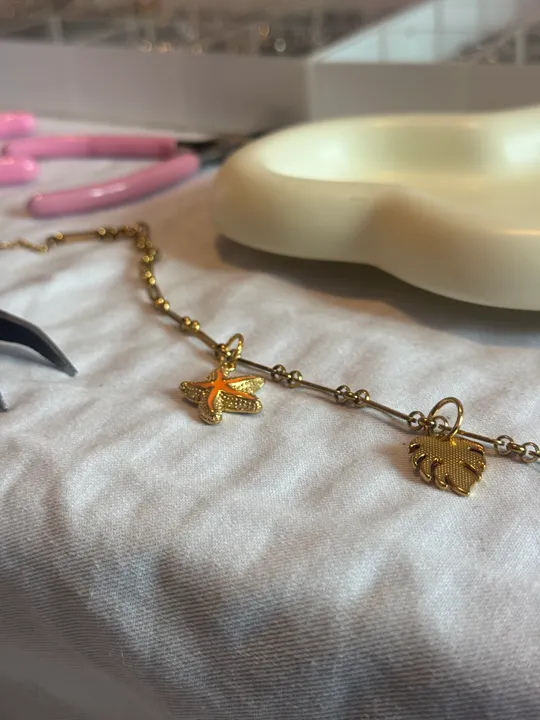 Goldene Halskette mit Seestern- und Blattanhängern.