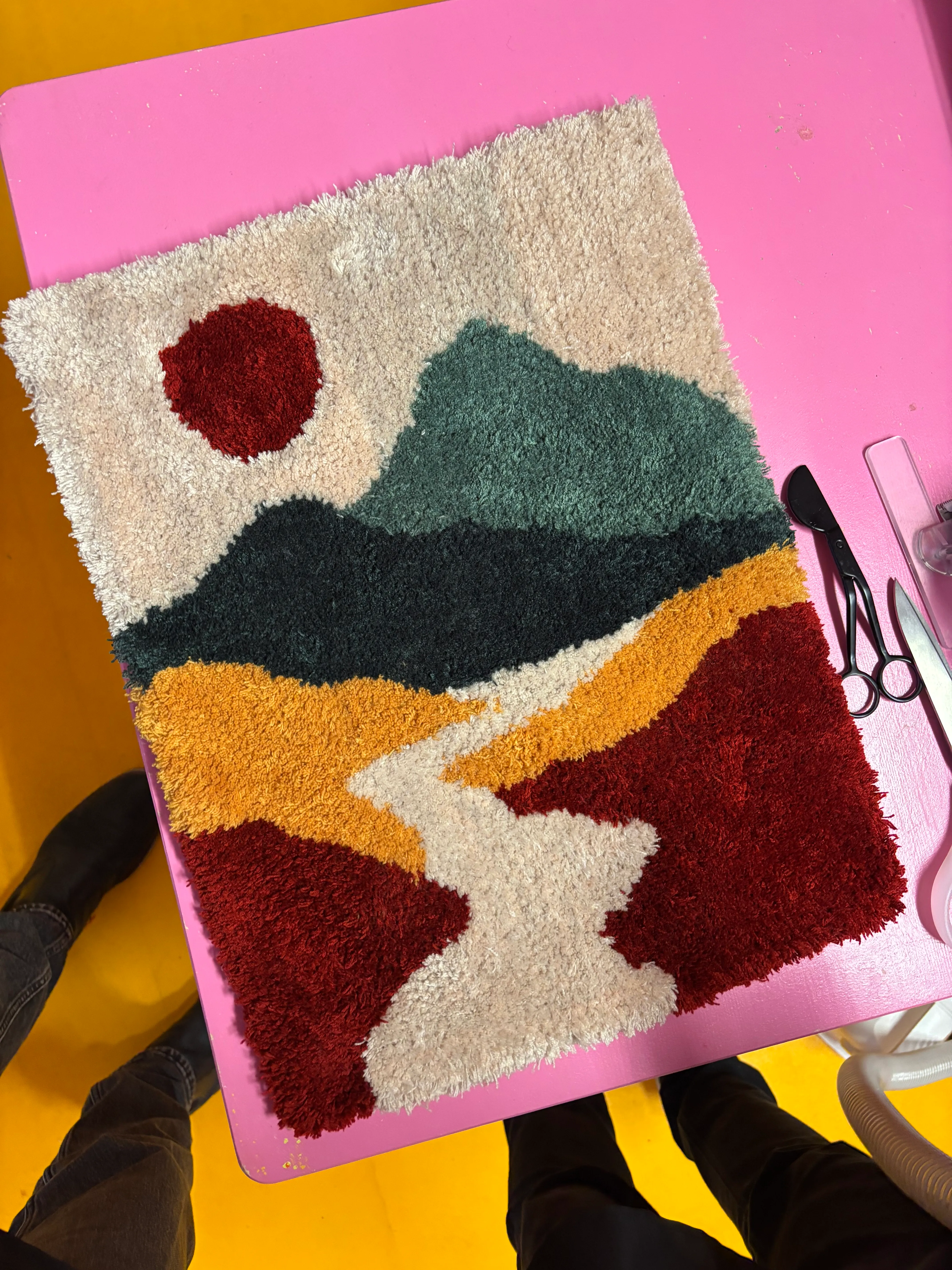 Bunter Teppich mit Berglandschaft auf pinkem Tisch.