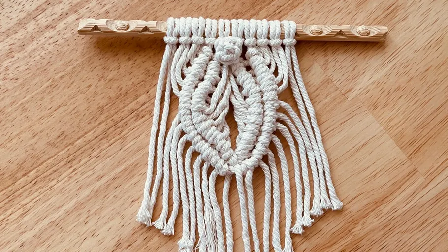 Macrame wall hanging from a wooden stick on a table surface