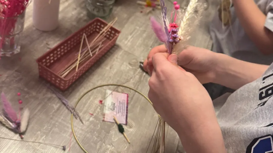Person crafting with dried flowers at table.